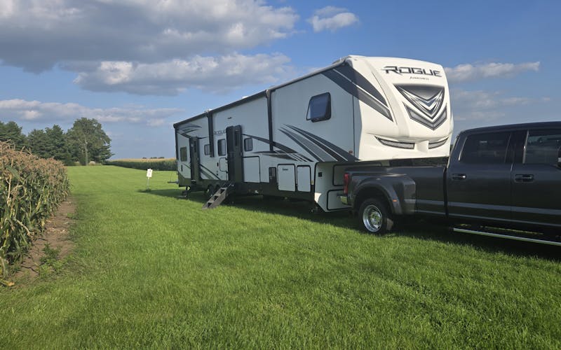 truck and fifth wheel camper parked in grass beside a corn field
