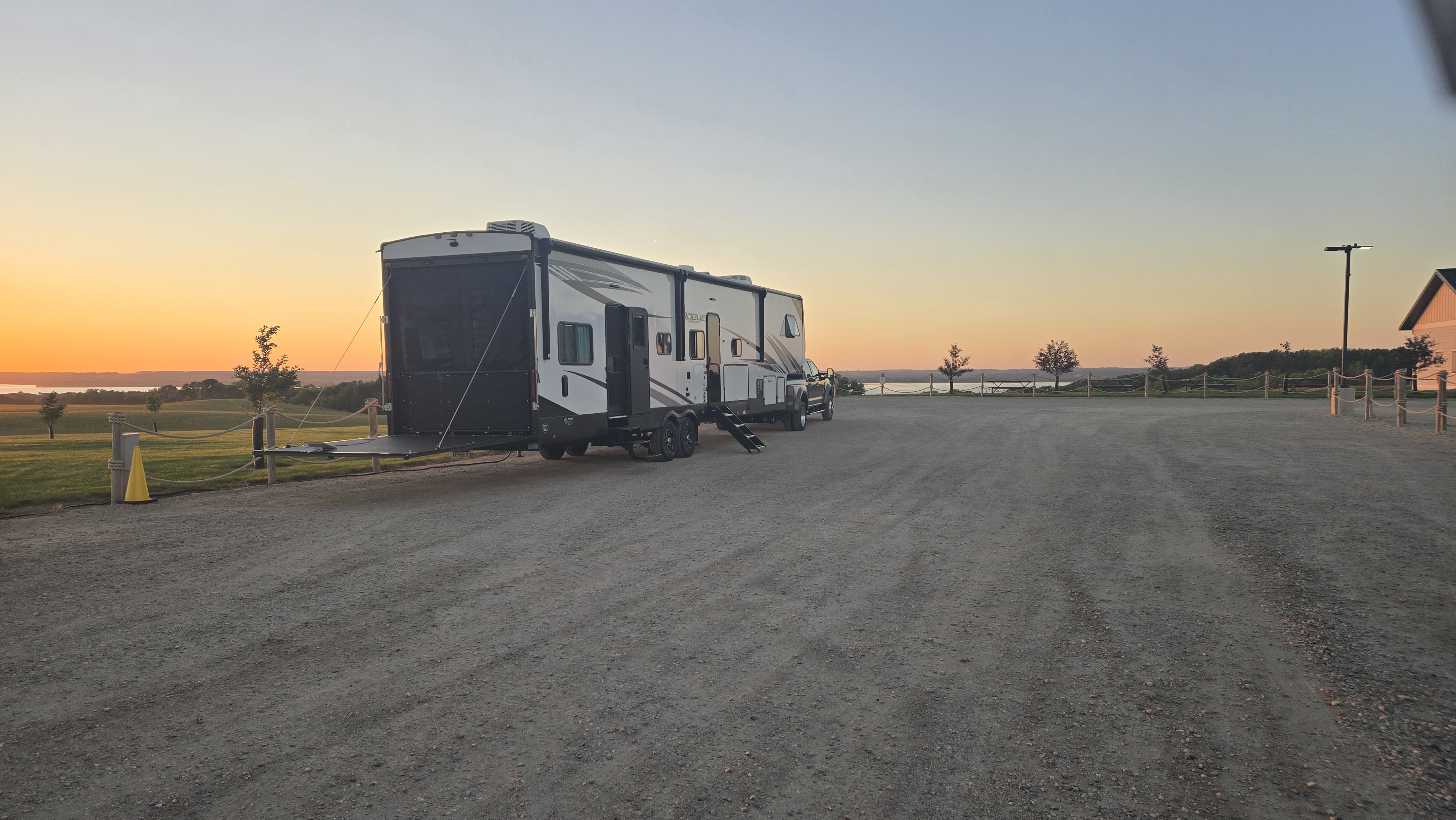 Camper parked in a gravel lot next to a winery with the sunset in the background