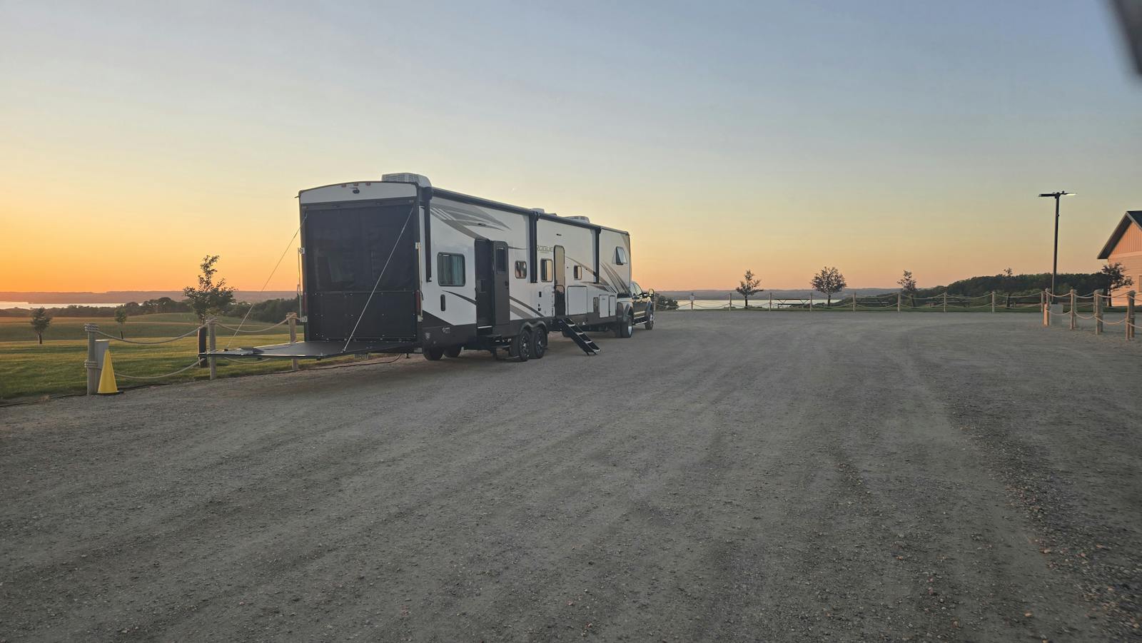 Camper parked in a gravel lot next to a winery with the sunset in the background