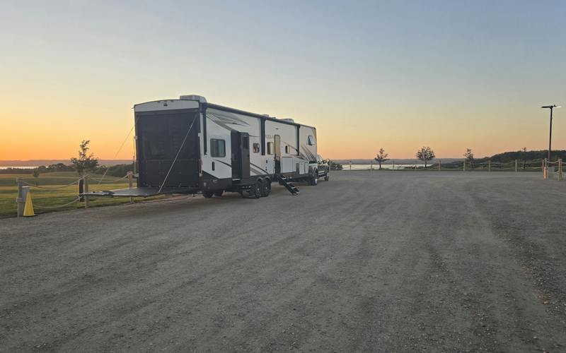 Camper parked in a gravel lot next to a winery with the sunset in the background