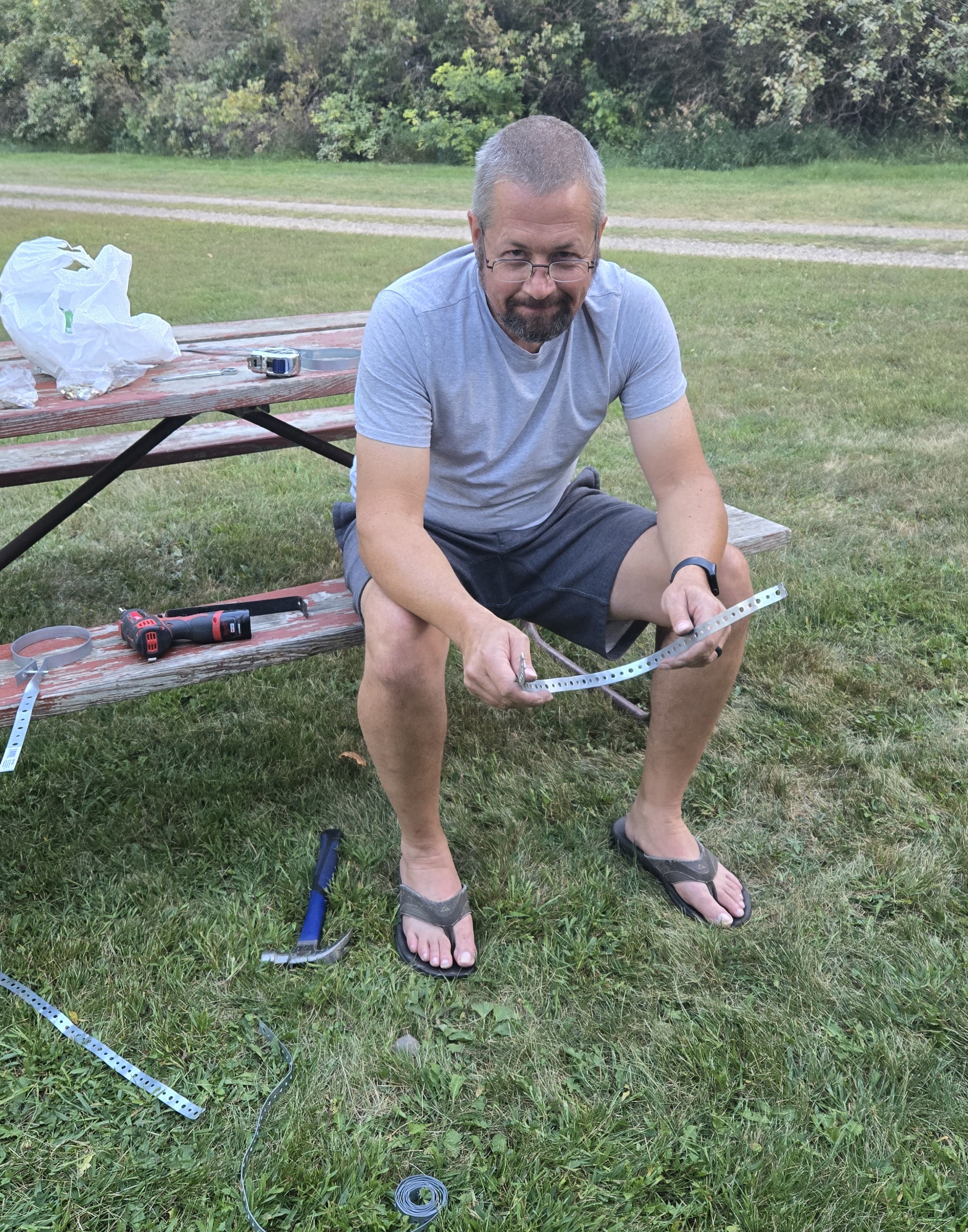 Jason sitting at a picnic table working on a thin piece of metal strapping