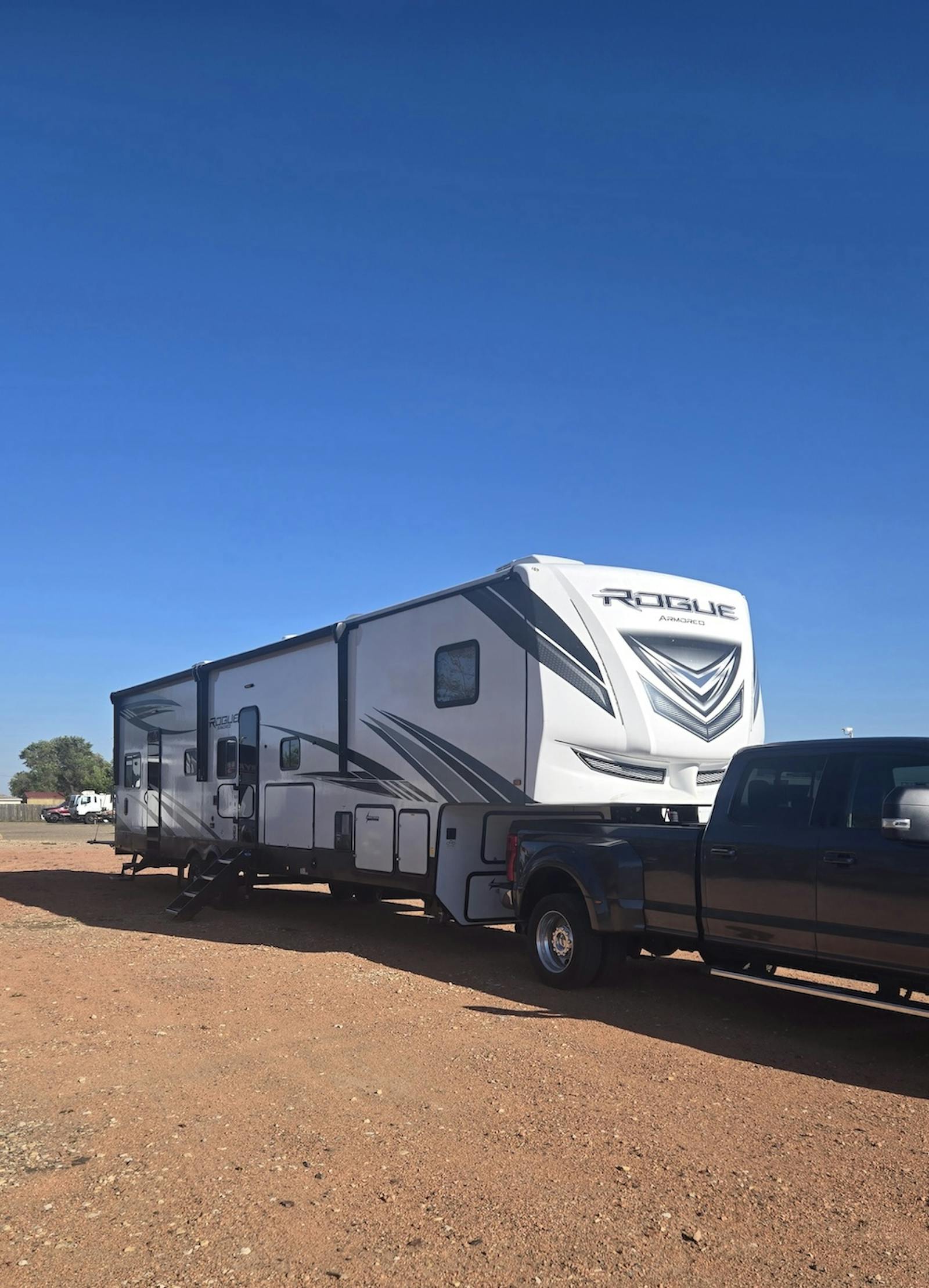 camper parked in a red gravel lot with blue clear sky behind it