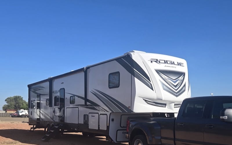 camper parked in a red gravel lot with blue clear sky behind it