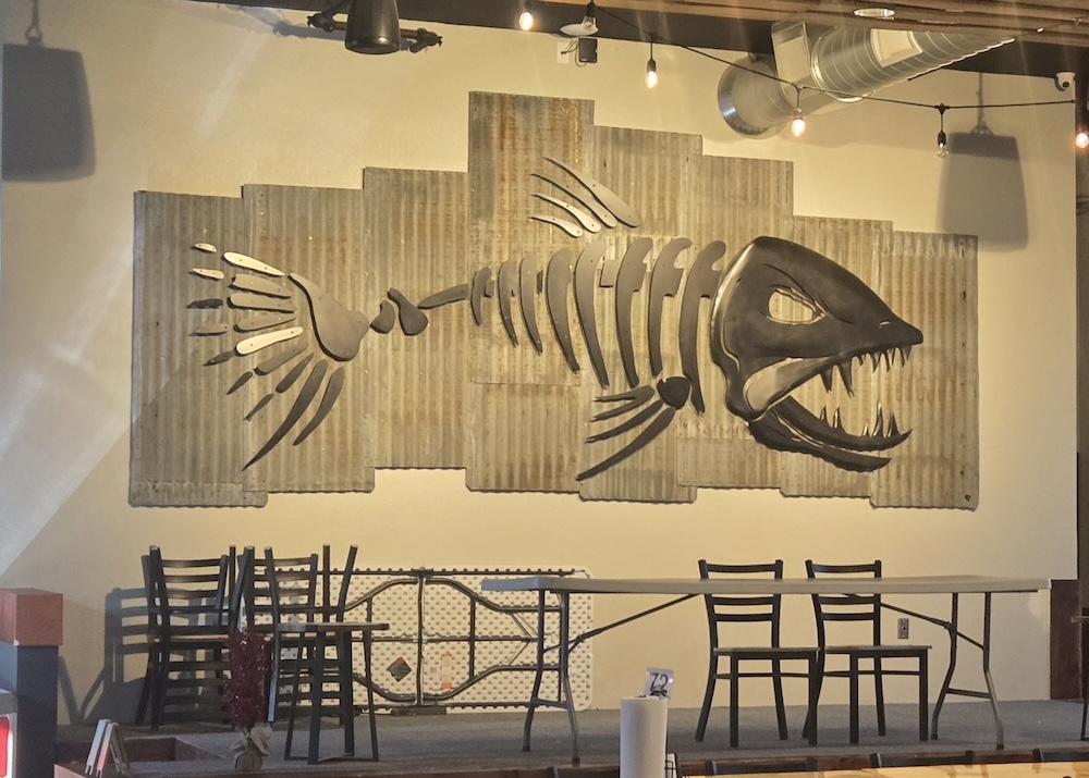 skeleton fish metal sculpture on wall behind tables in a brewery