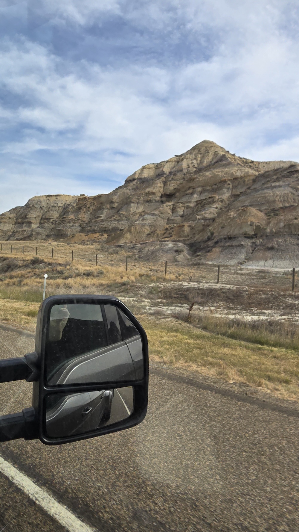 rocky hill and pillar formations with grey and red striations taken from truck window with truck mirror in foreground
