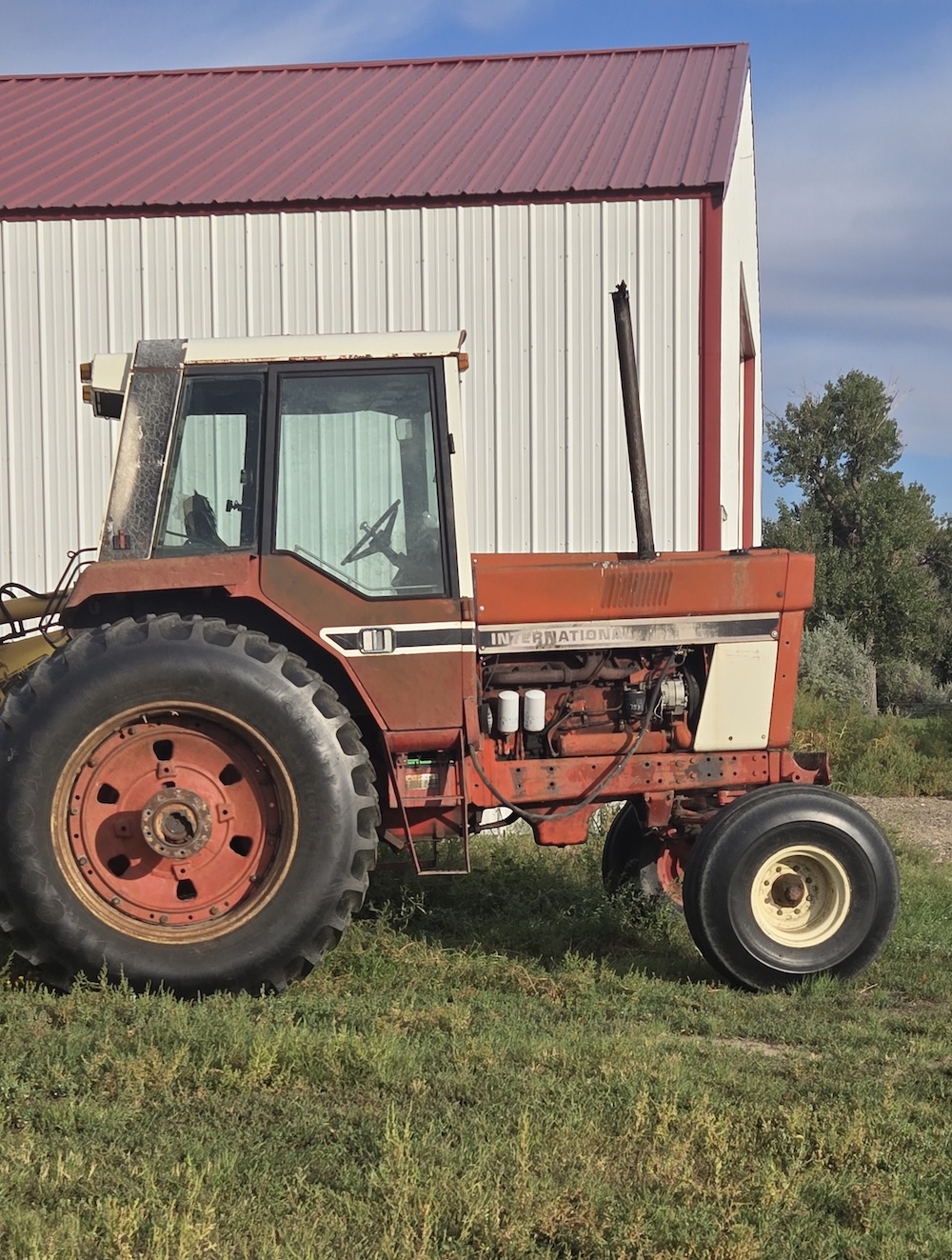 an old red and white farm tractor parked in front of a tin shed
