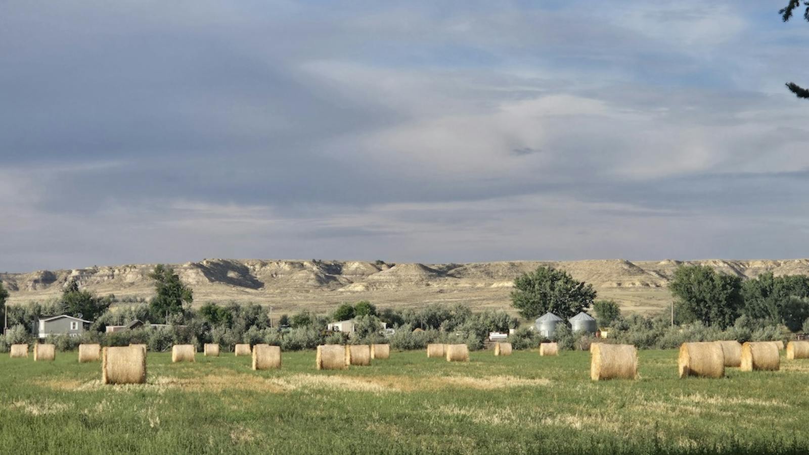 a field of hay bales with rocky hills in the background and a cloudy sky