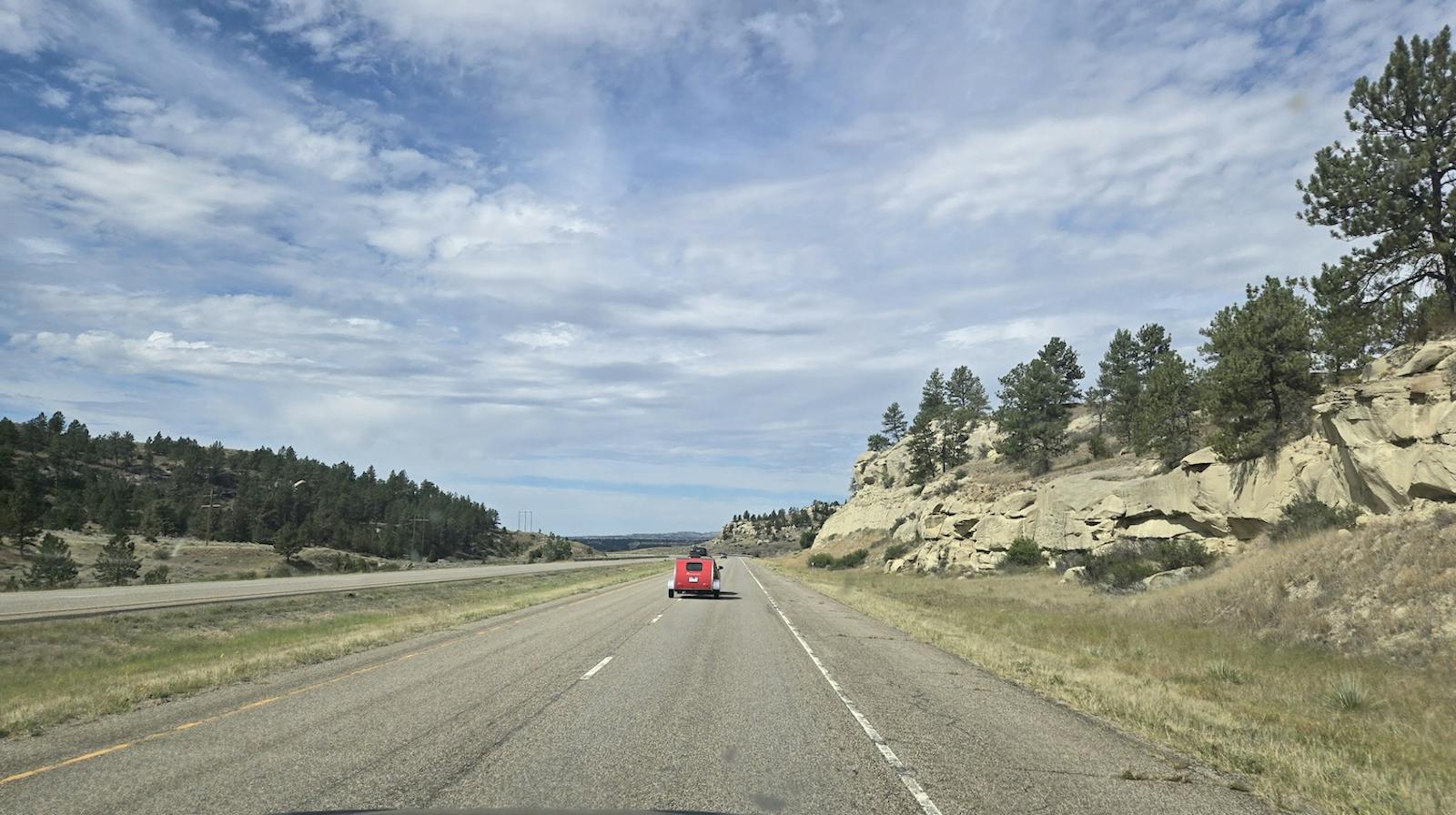 montana highway with rocky hills left and right and a car towing a small red camper ahead