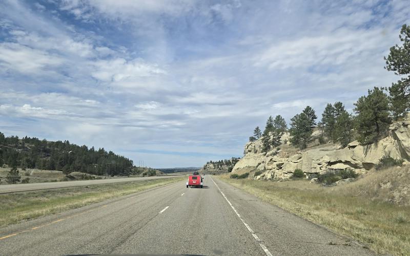 montana highway with rocky hills left and right and a car towing a small red camper ahead