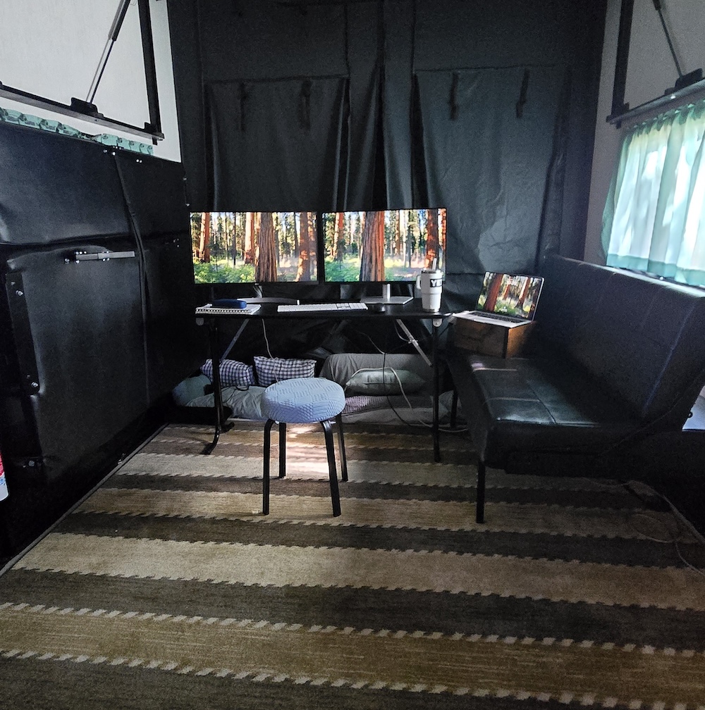 camper garage office with desk facing the rear and two large monitors plus laptop and a kitchen stool for chair