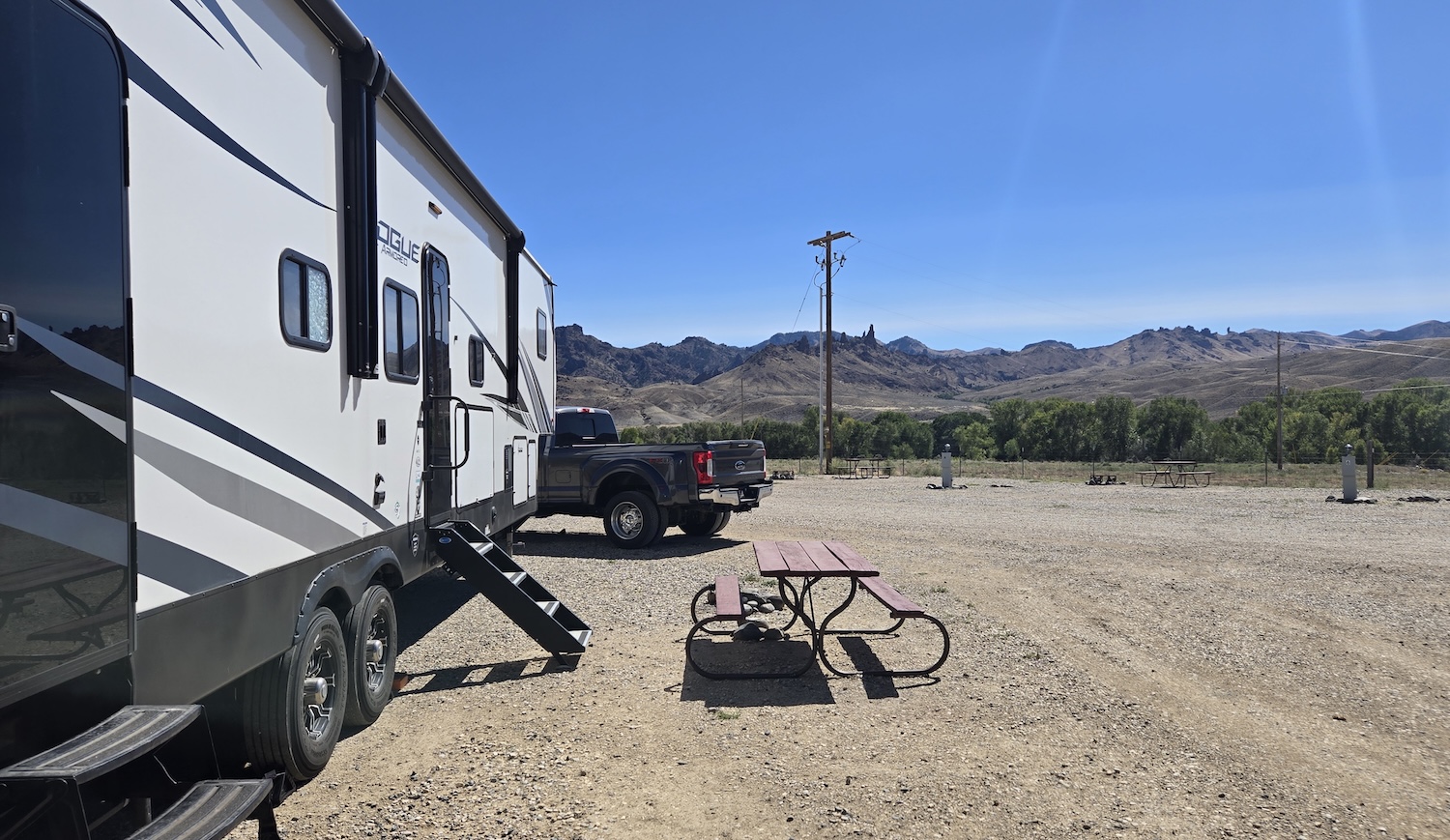 view from the side of our camper in a dirt and stone campground lot with mountains in background