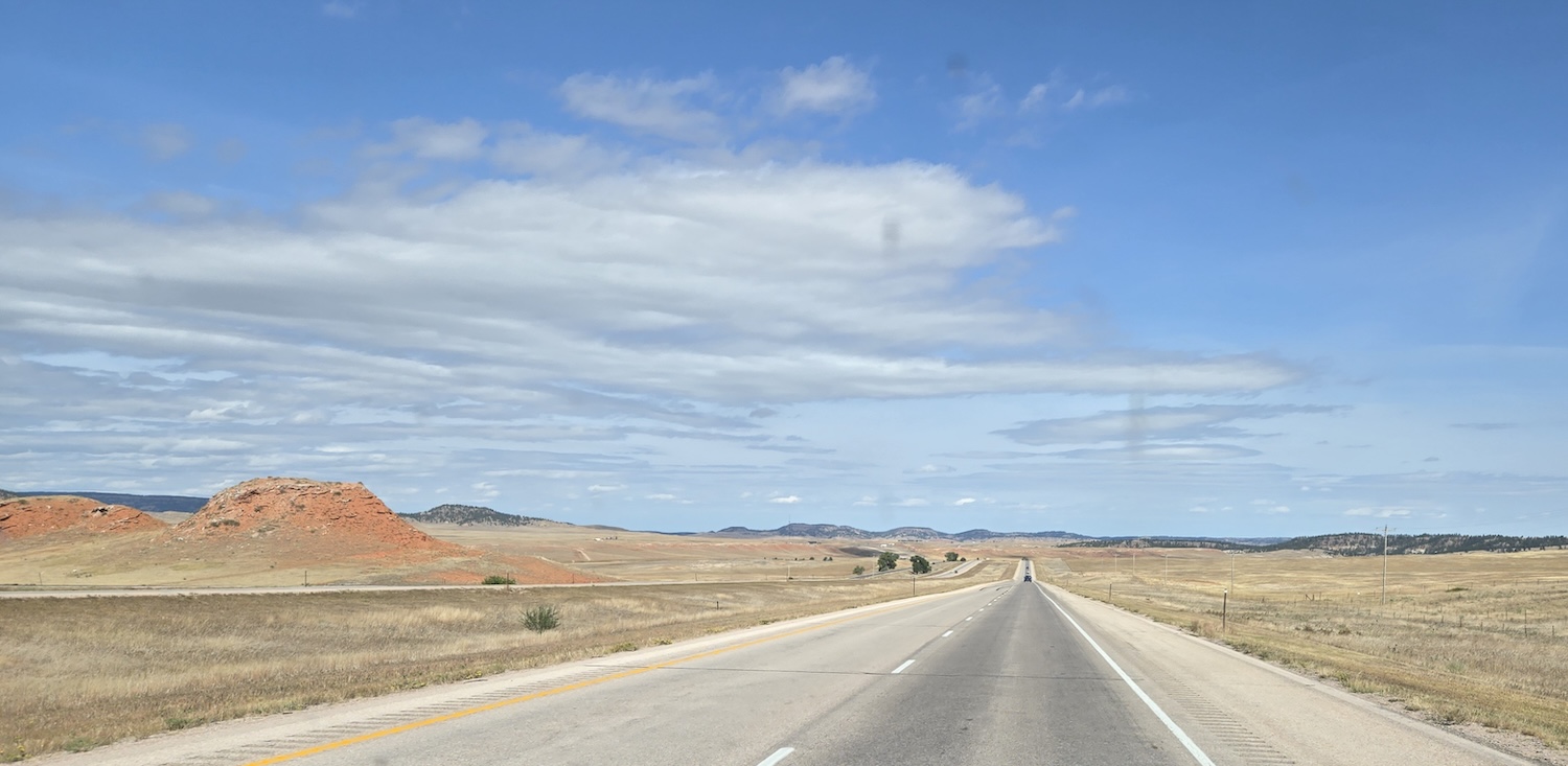 a highway seen through vehicle windshield with brown plains and salmon colored hills to the sides
