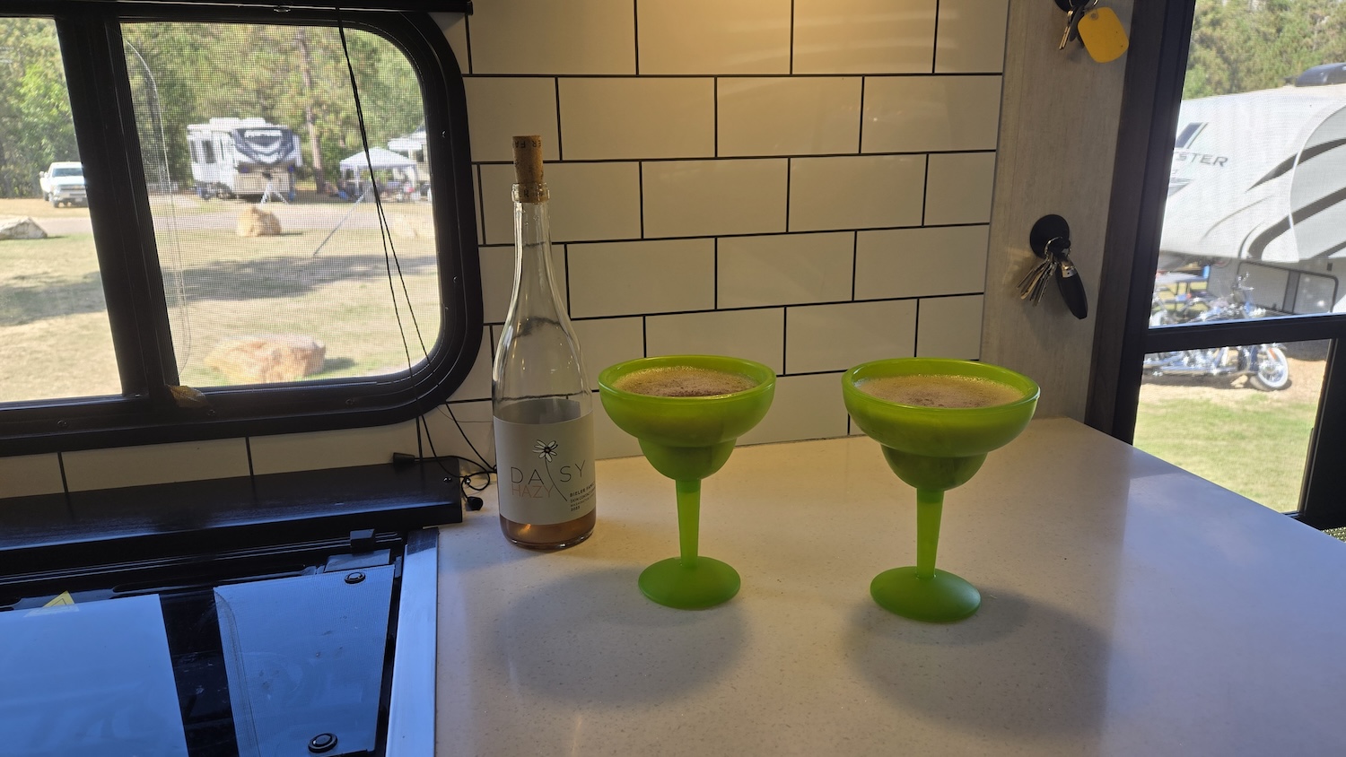 wine slushies in green margarita glasses sitting next to a bottle of wine on camper counter