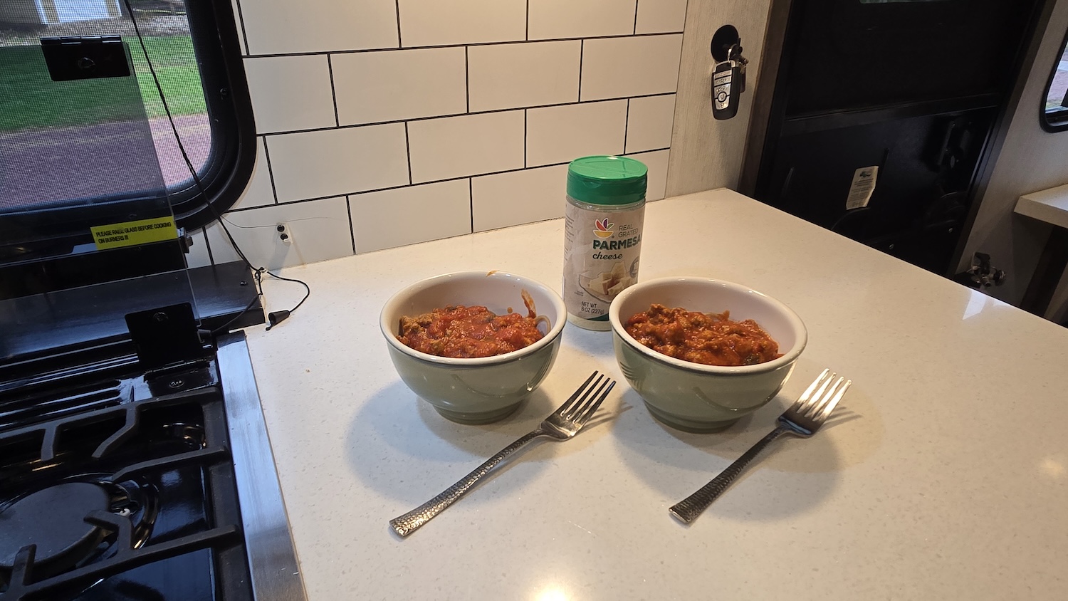 two bowls of spaghetti with meat sauce, two forks and packaged parmesan cheese on camper counter
