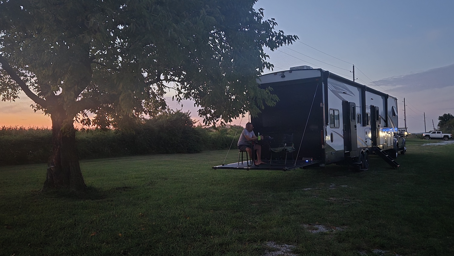 camper parked in shade of old fruit tree sunset in background