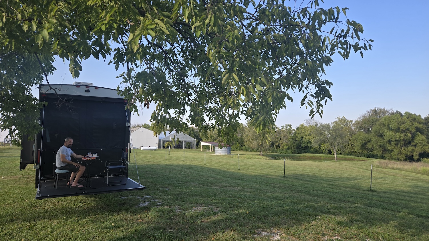camper parked in shade of old fruit tree with toy hauler deck down and Jason on deck