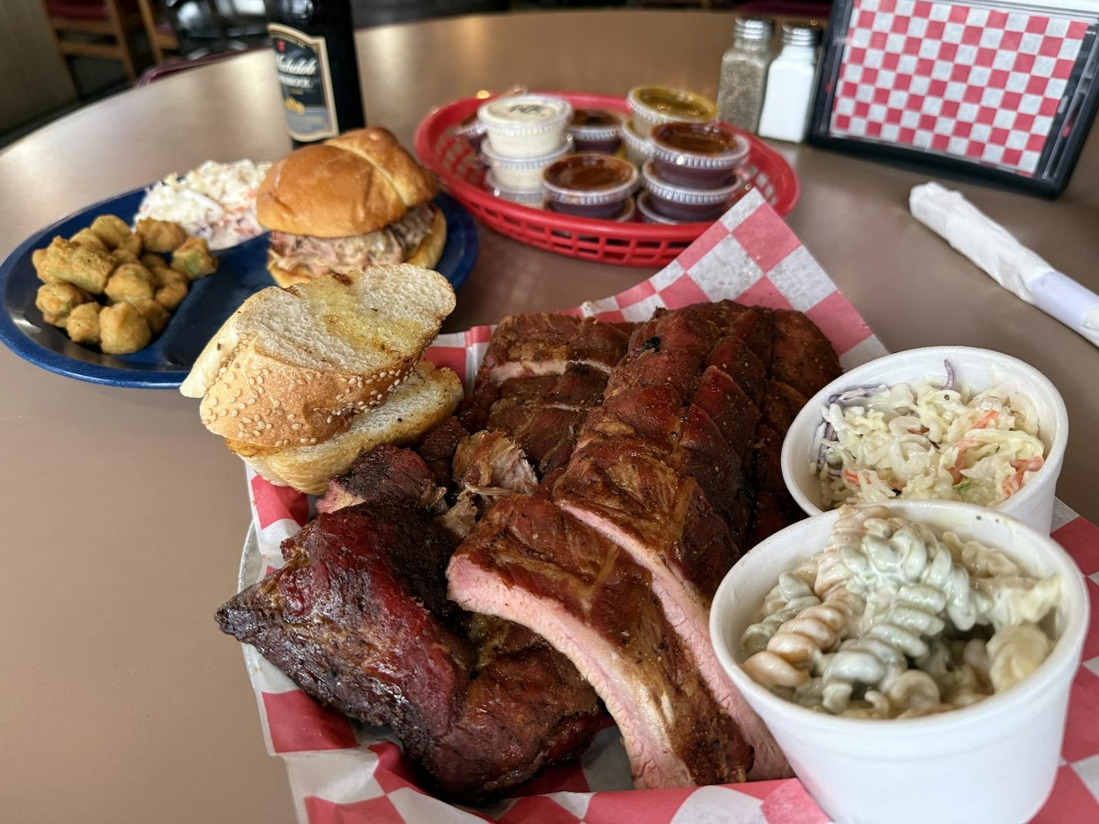a plate of BBQ ribs with sides of pasta salad and coleslaw, another sandwich sides and sauces in background