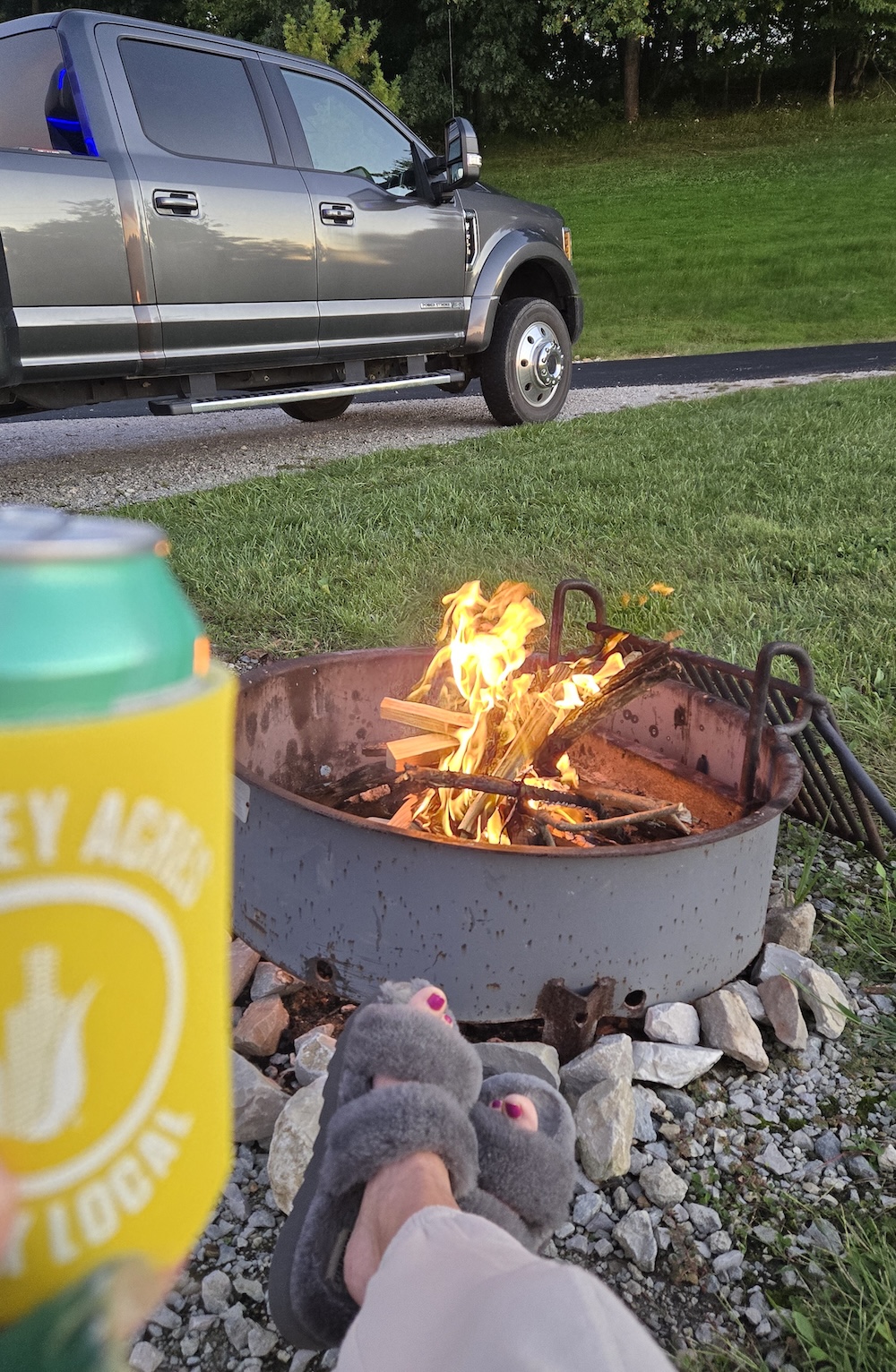 a firepit with a blazing fire in the background my feet in fuzzy slippers and a beer in foreground