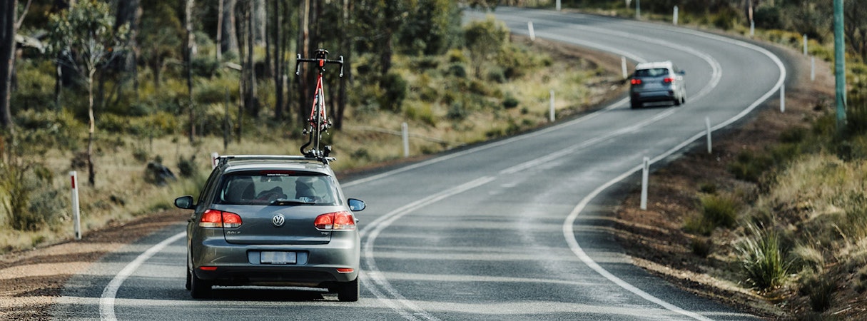 VW Hatchback with bike on roof racks driving on rural highway