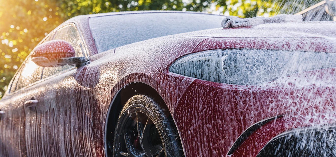Red sedan being washed by hand