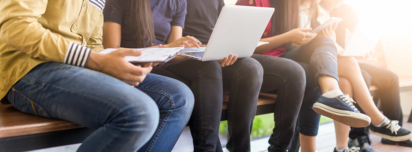 Kids sitting on bench with laptops and notebooks