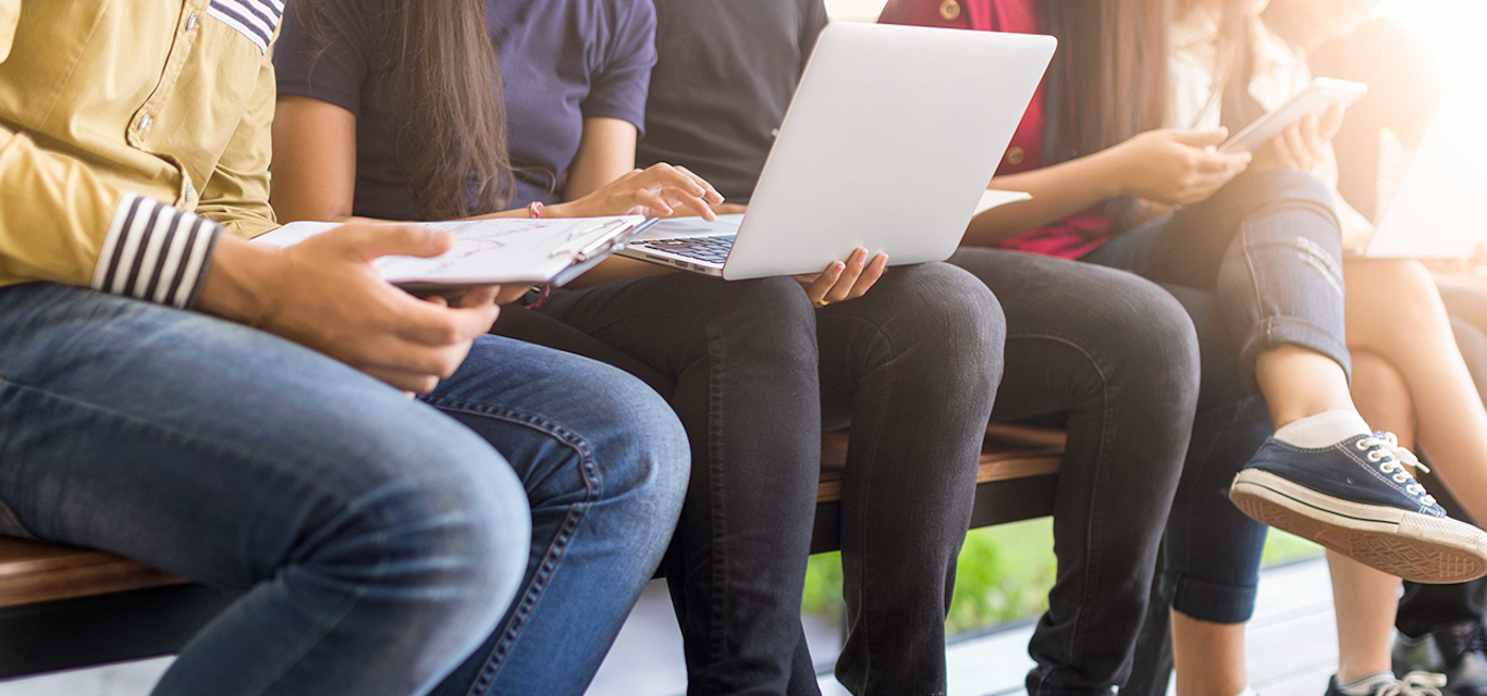 Kids sitting on bench with laptops and notebooks