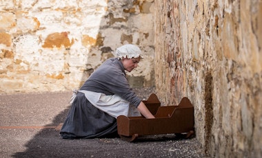 woman dressed as a convict kneeling over a wooden crib