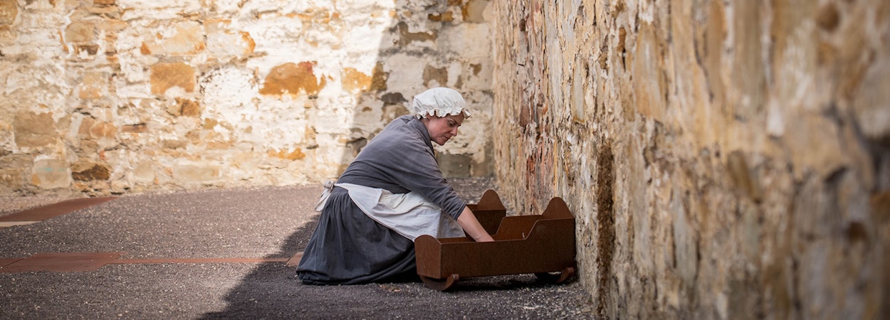 woman dressed as a convict kneeling over a wooden crib