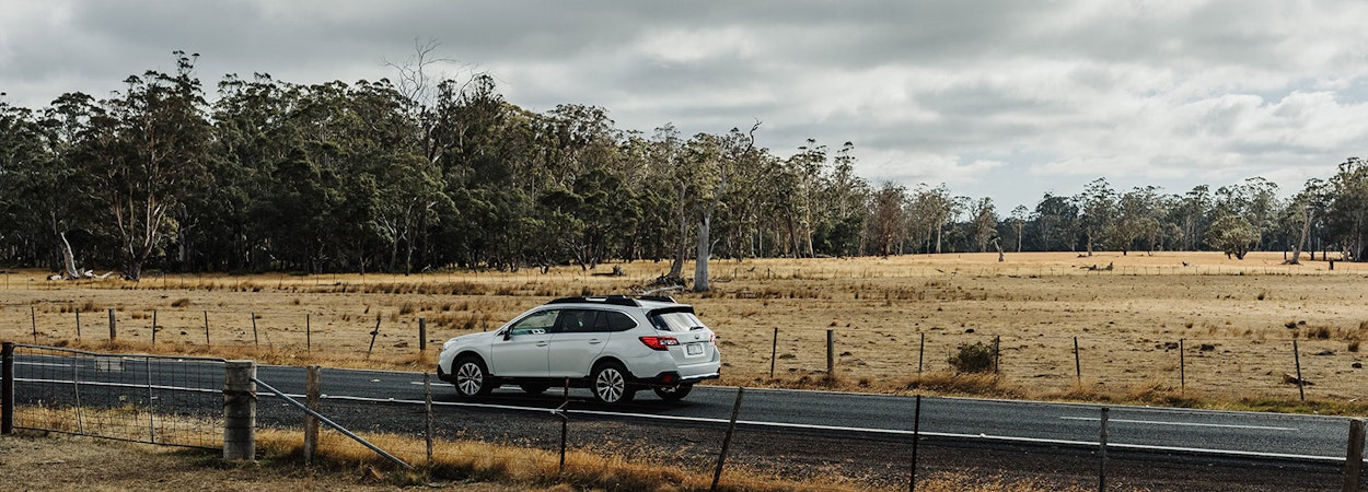 White Subaru Outback driving along a rural road