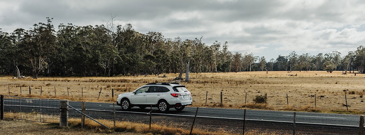 White Subaru Outback driving along a rural road