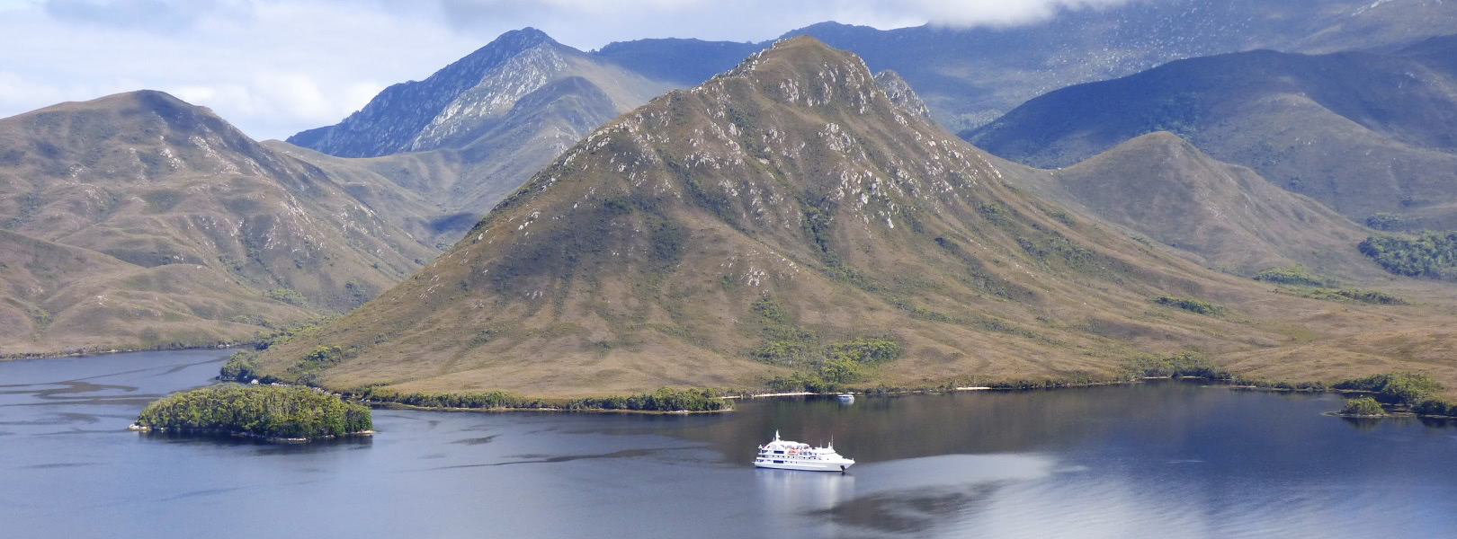 Small crusie ship off the coast of a mountainous region.