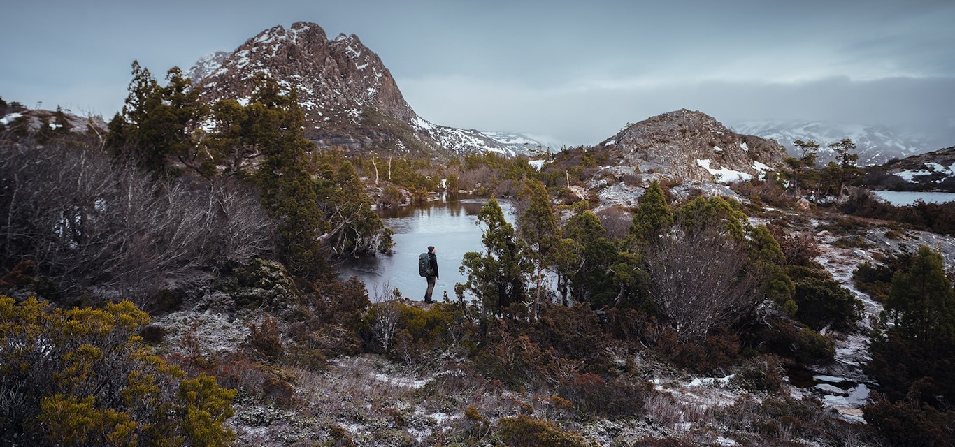 A man stands at the edge of a lake at Cradle Mountain