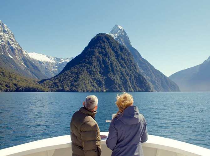 Two people on a boat looking out over New Zealand water at mountains