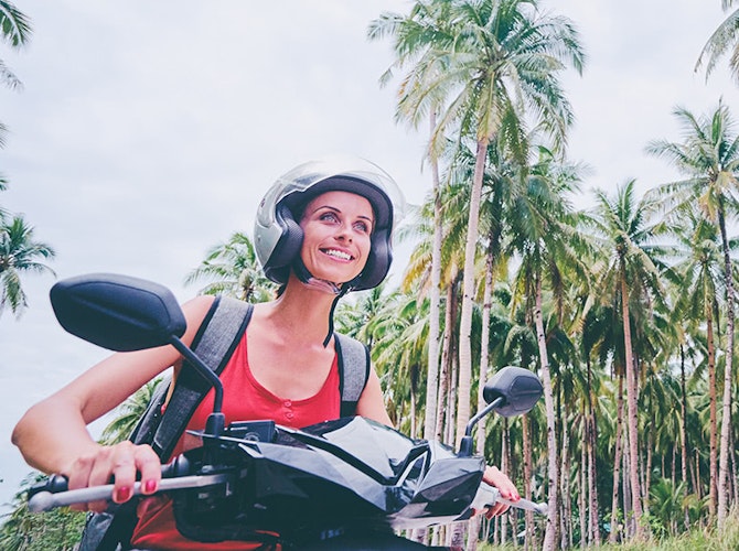 Person riding scooter along road lined with palm trees