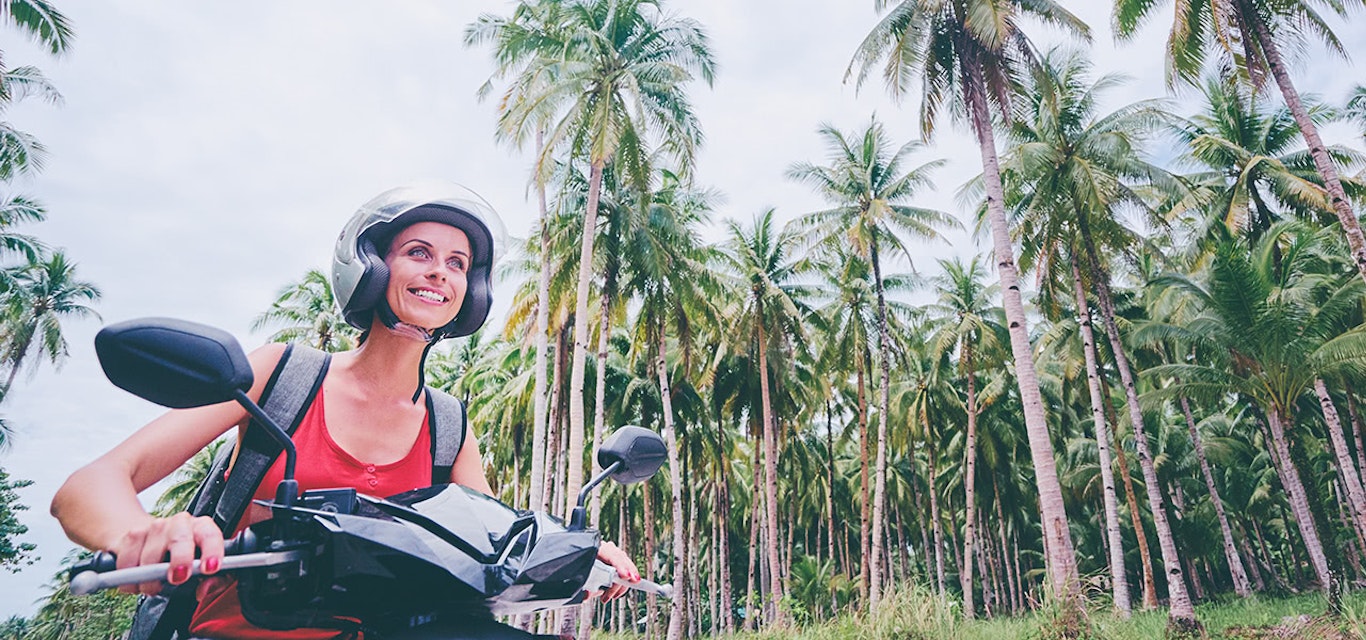 Person riding scooter along road lined with palm trees