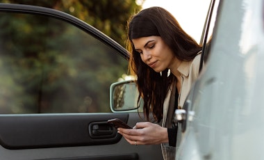 Woman sitting in car with door open looking at mobile phone