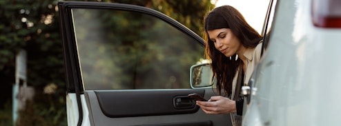 Woman sitting in car with door open looking at mobile phone