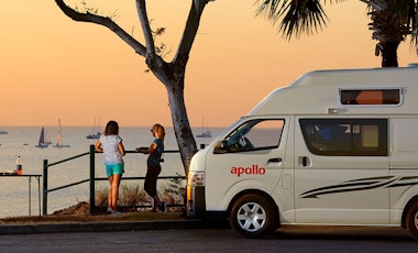 Two women enjoying the view of the bay next to an Apollo van
