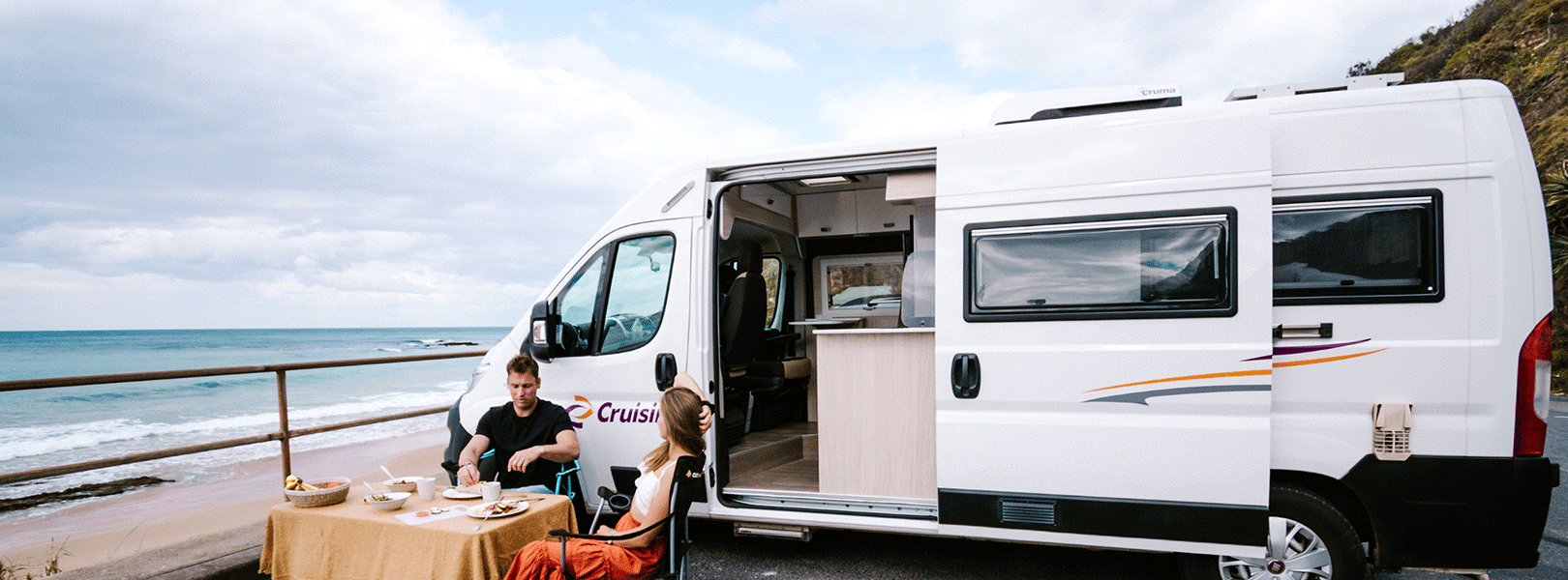 Young couple enjoying a beachside breakfast next to their motorhome