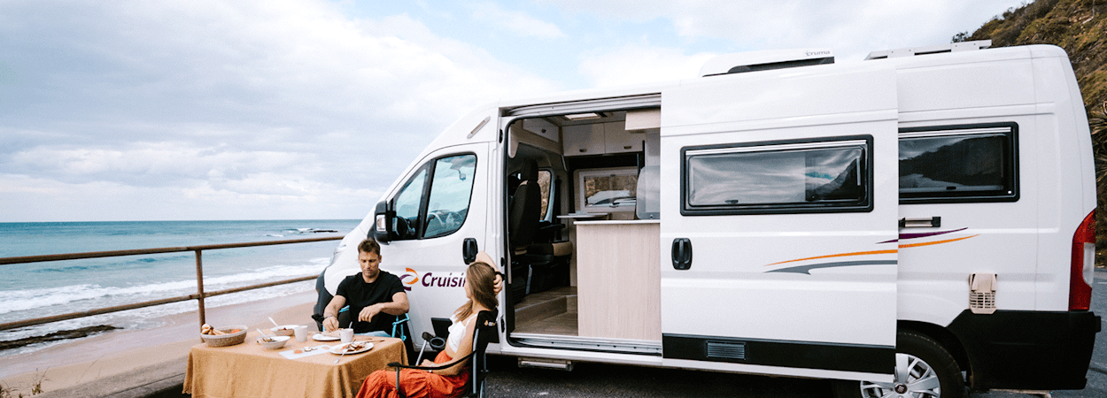 Young couple enjoying a beachside breakfast next to their motorhome