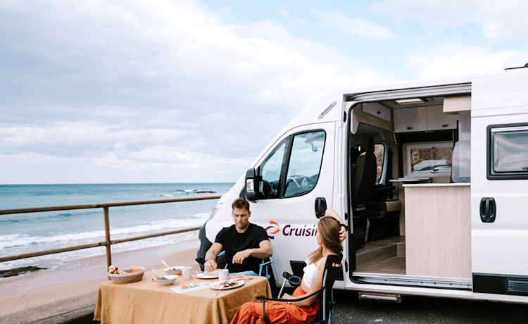 Young couple enjoying a beachside breakfast next to their motorhome
