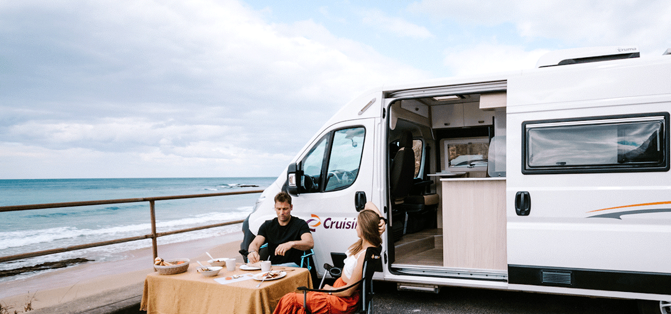 Young couple enjoying a beachside breakfast next to their motorhome