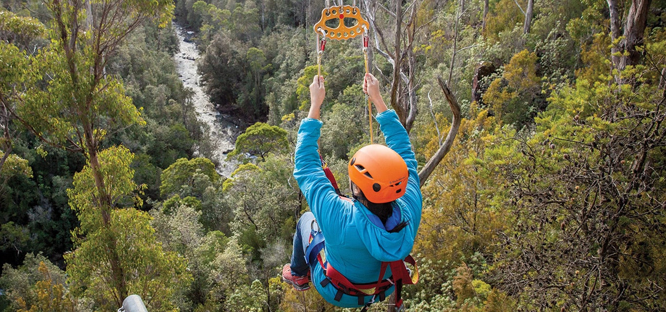 Person on a zip line high above trees and a river