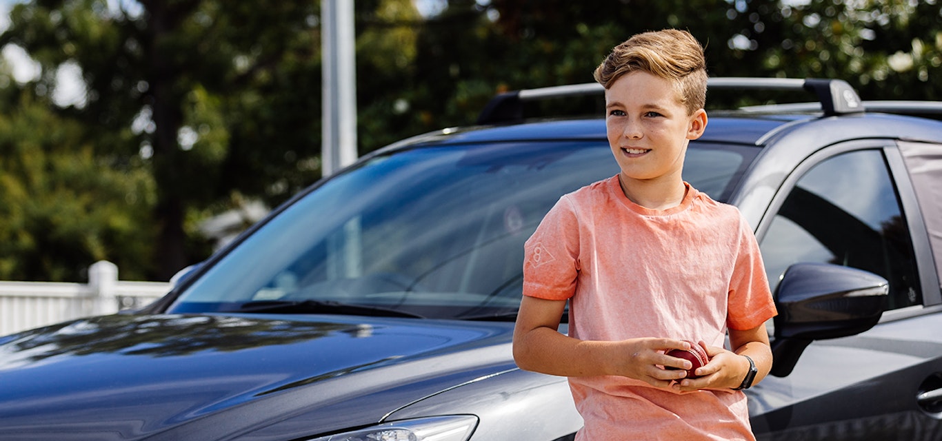 Boy holding cricket ball leaning on car