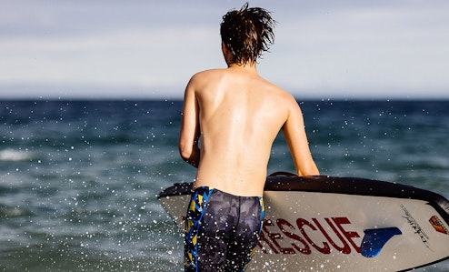 Young surfer heading out into the ocean with his board