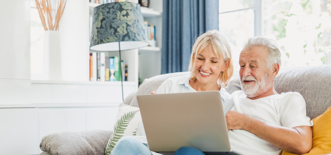 Couple senior using computer laptop on sofa at home for online shopping, surfing internet