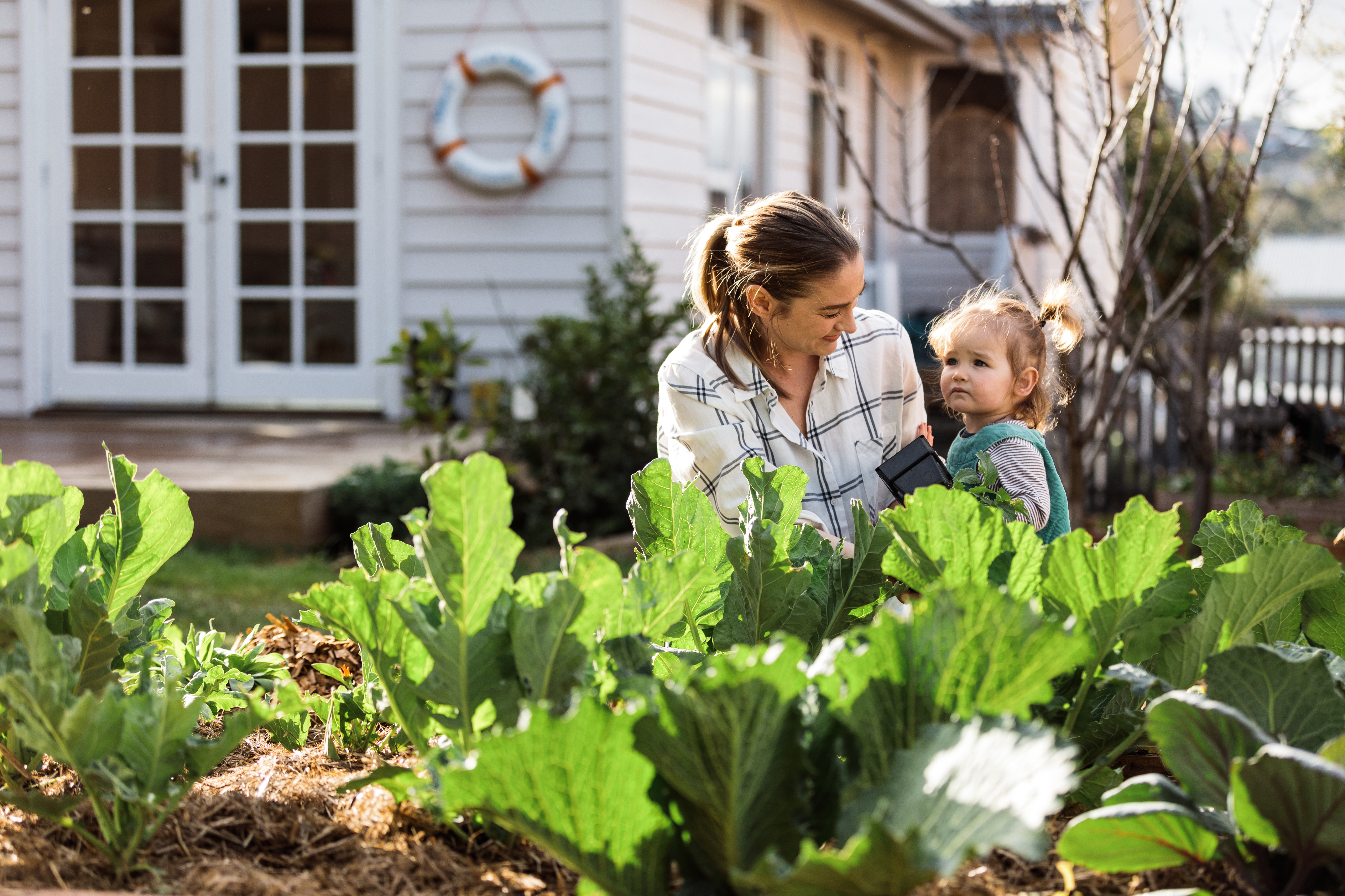 Parent and child smiling in front of vegetable patch