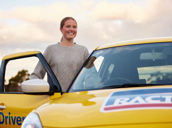 Female learner driver standing at door of car