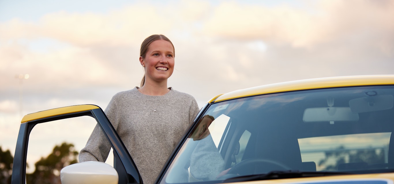 Female learner driver standing at door of car