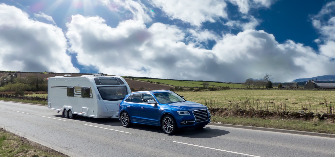 Blue car travelling on road with caravan.
